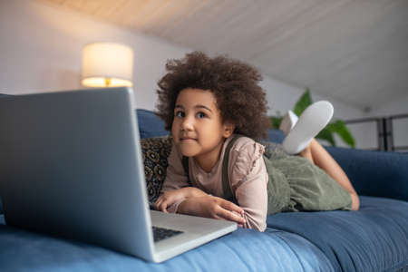 Little girl lying on couch near laptop