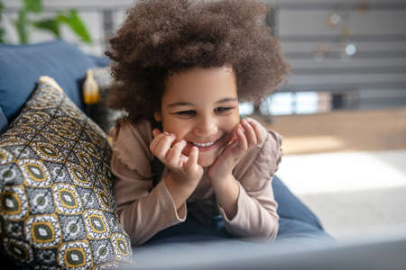 Cute joyful little girl lying on couch on stomachの写真素材