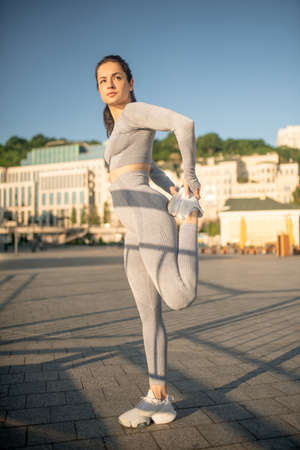 Young female sportsperson stretching her legs and looking concentrated