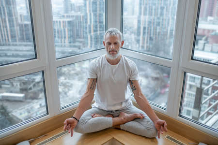 Gray-haired man in a white tshirt doing yoga and looking concentrated