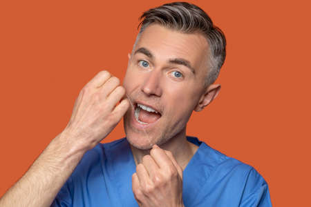 Cute gray-eyed man using dental floss