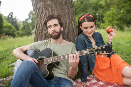 Guy playing guitar and girl eating apple