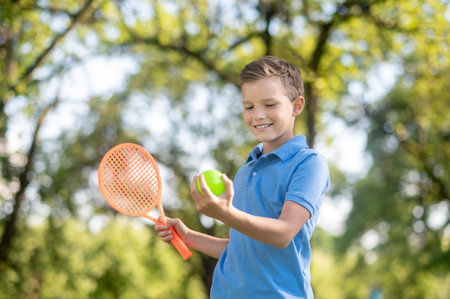 Smiling boy looking at tennis ball in handの写真素材