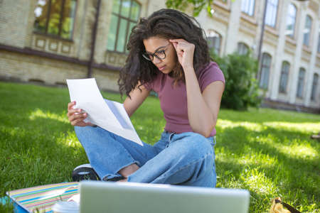 Cute young dark-skinned girl preparing to exams in the park