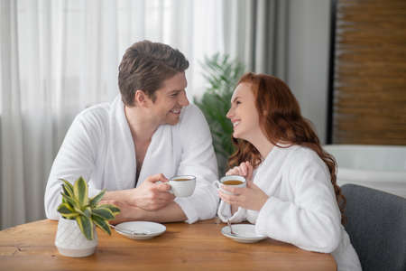 A couple in white bathrobes having coffee and feeling happyの写真素材