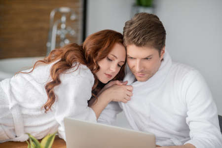 Ginger woman in a white bathrobe and her husband looking happy and in love