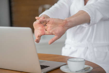Close up picture of a man sitting at the laptop and stretching his arms