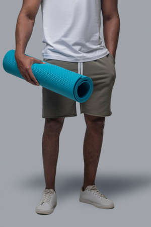 A man in a white tshirt with a blue mat in hands