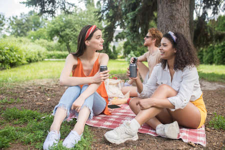 Two girls with drink and guy behind in natureの写真素材