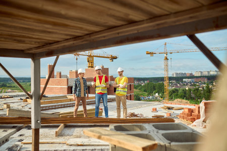 Three workers in hardhats having a conversation on the construction siteの写真素材