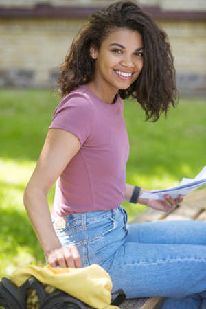 A cute girl in a pink tshirt sitting on the grass in the parkの写真素材