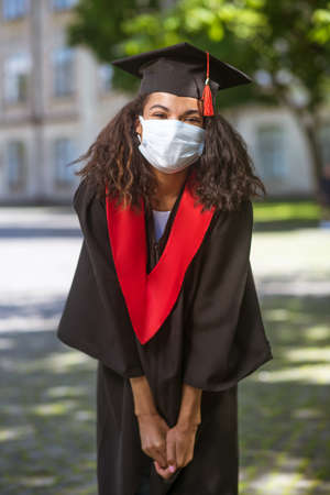 A dark-skinned cute girl in academic cap and in a preventive maskの写真素材