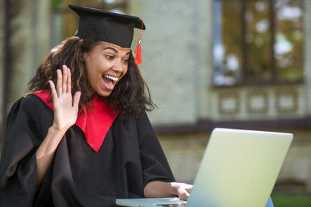 A cute graduate in academic gown having a vieo call and feeling happy