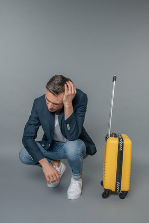 Sad man crouched near his suitcaseの写真素材