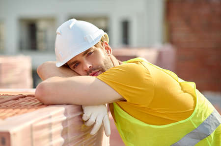 Sad tired builder in a protective helmet resting after hard work