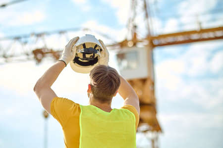 Worker in cotton gloves lifting his protective helmet in the airの写真素材