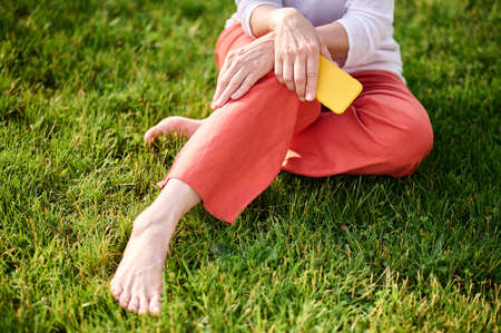 Barefoot woman sitting with smartphone on grass