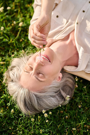 Woman with flower in hand lying on lawnの写真素材