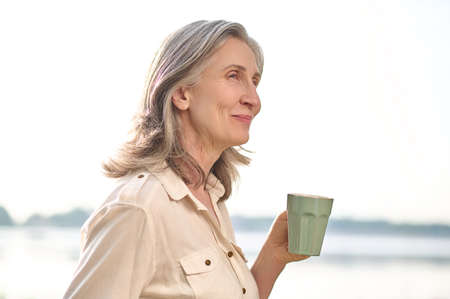 Smiling woman with a cup of coffee in nature