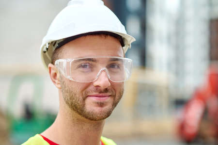 Pleased attractive builder in safety goggles posing for the cameraの写真素材