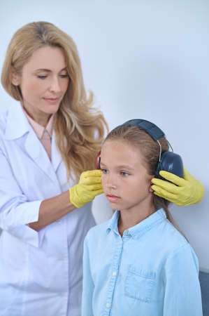 Woman otolaryngologist putting headphones on to school-age girlの写真素材