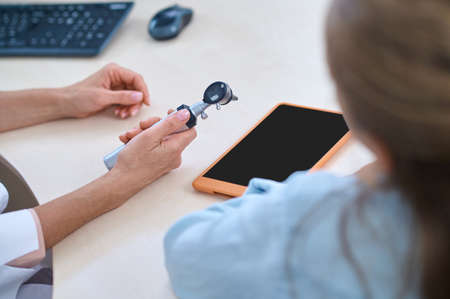 Hands of doctor with otoscope and patient