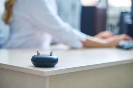 Hearing aid on table and doctor working at laptop