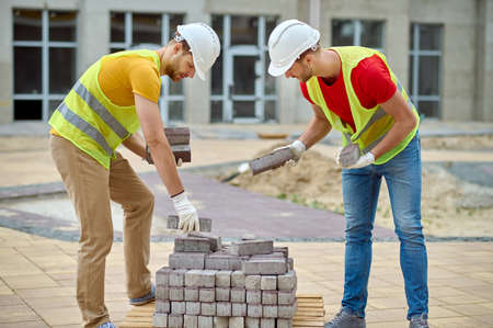 Skilled builders in cotton gloves choosing construction materials for pavementの写真素材