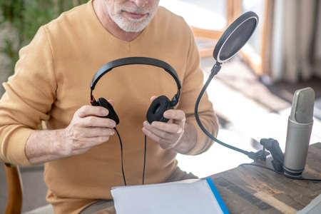 A gray-haired man in black headphones speaking in microphoneの写真素材