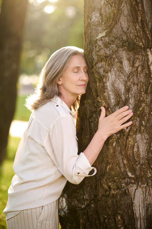 Woman with closed eyes touching treeの写真素材