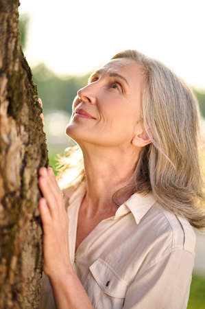 Smiling woman looking pensively up at treeの写真素材