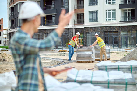 Two young builders looking at their colleague waving at themの写真素材