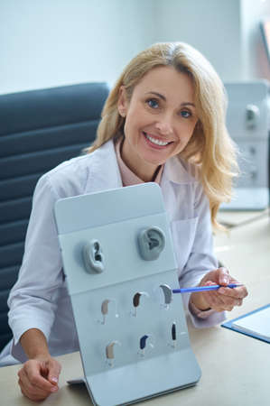 Cheerful otorhinolaryngologist pointing with a pen at listening apparatuses