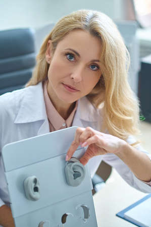 Experienced professional otolaryngologist demonstrating how to wear a hearing aid