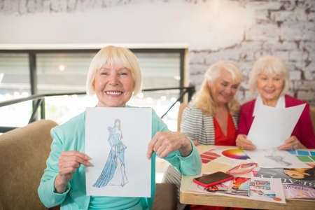 A blonde woman in a blue suit showing a sketch with a new dress