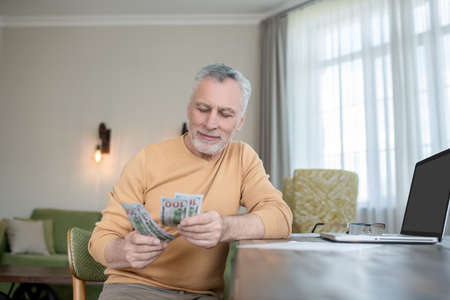 Gray-haired man standing and counting money