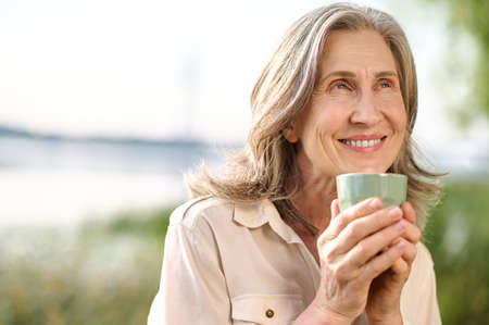Optimistic smiling woman with coffee outdoors