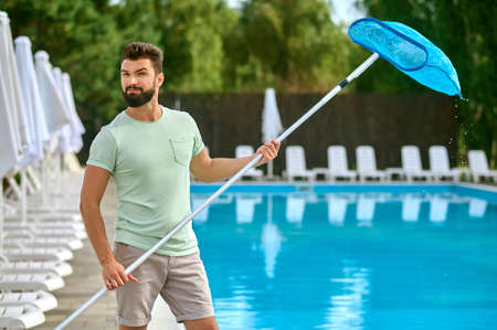 A dark-haired man cleaning the swimming pool and looking busyの写真素材