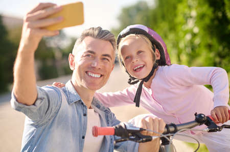 Daughter with bike and dad taking selfie on smartphoneの写真素材
