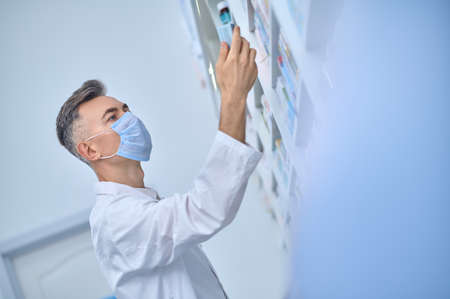 Pharmacist in protective mask considering medication with interest