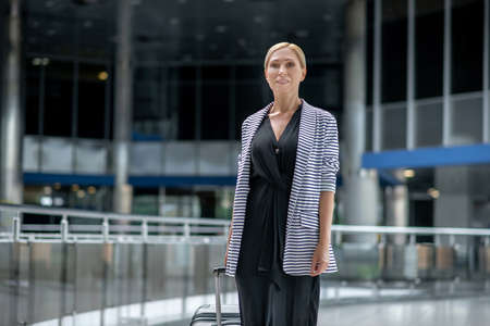 Smiling woman with suitcase walking in airportの写真素材