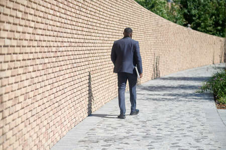 A dark-skinned man walking along the brick wallの写真素材