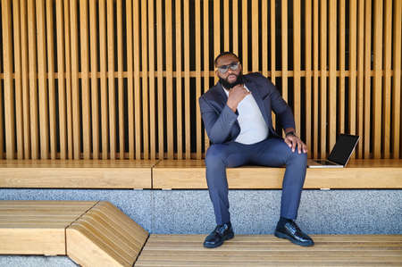 A dark-skinned businessman with a laptopsitting on the bench and workingの写真素材
