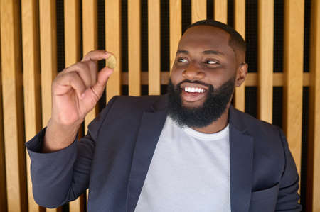 A bearded dark-skinned man holding a bitcoinの写真素材