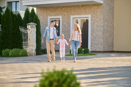 Little girl with parents walking near new buildingの写真素材