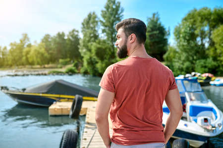 A dark-haired man standing on a dock near the boatの写真素材