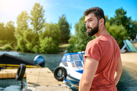 A dark-haired man standing on a dock near the boatの写真素材