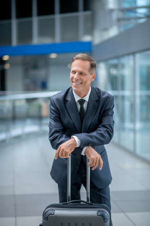 Cheerful man leaning on suitcase at airportの写真素材