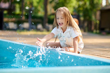 A blonde little girl sitting near the swimming poolの写真素材