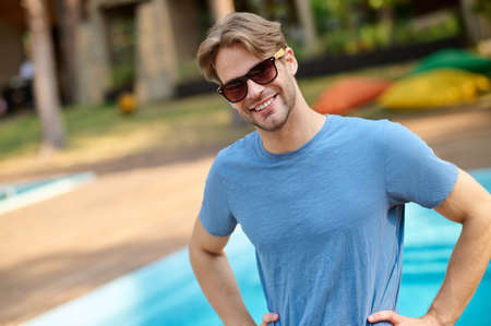A young man in a blue tshirt and sunglasses near swimming poolの写真素材